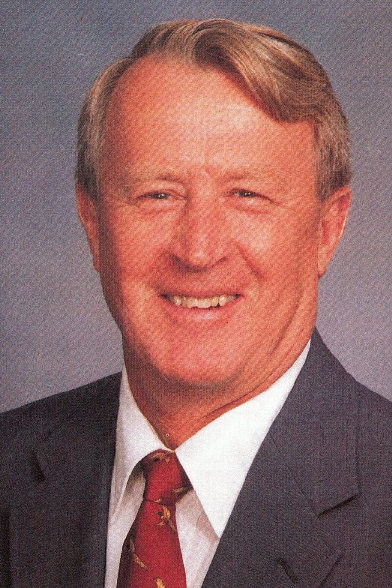 Photo of an older man, smiling at the camera and wearing a suit and tie