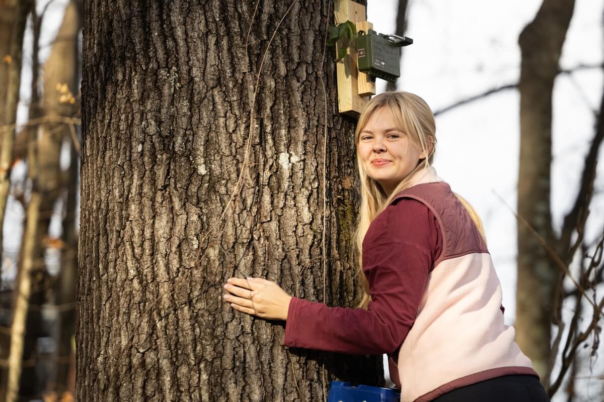 Photo of Molly Bailey in front of an echolocation recorder, smiling at the camera