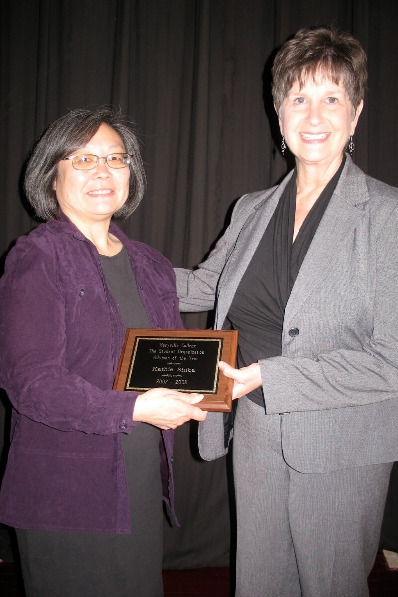 Photo of Dr. Kathie Shiba holding a plaque beside Vandy Kemp