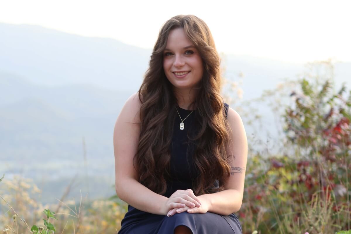 Photo of Dana Patterson sitting on a wall with the mountains in the background, smiling