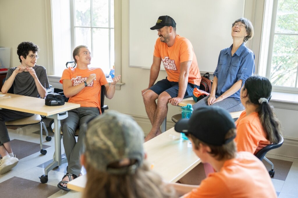 Photo of a woman leaning back and laughing as she listens to teens talk about summer camp experiences