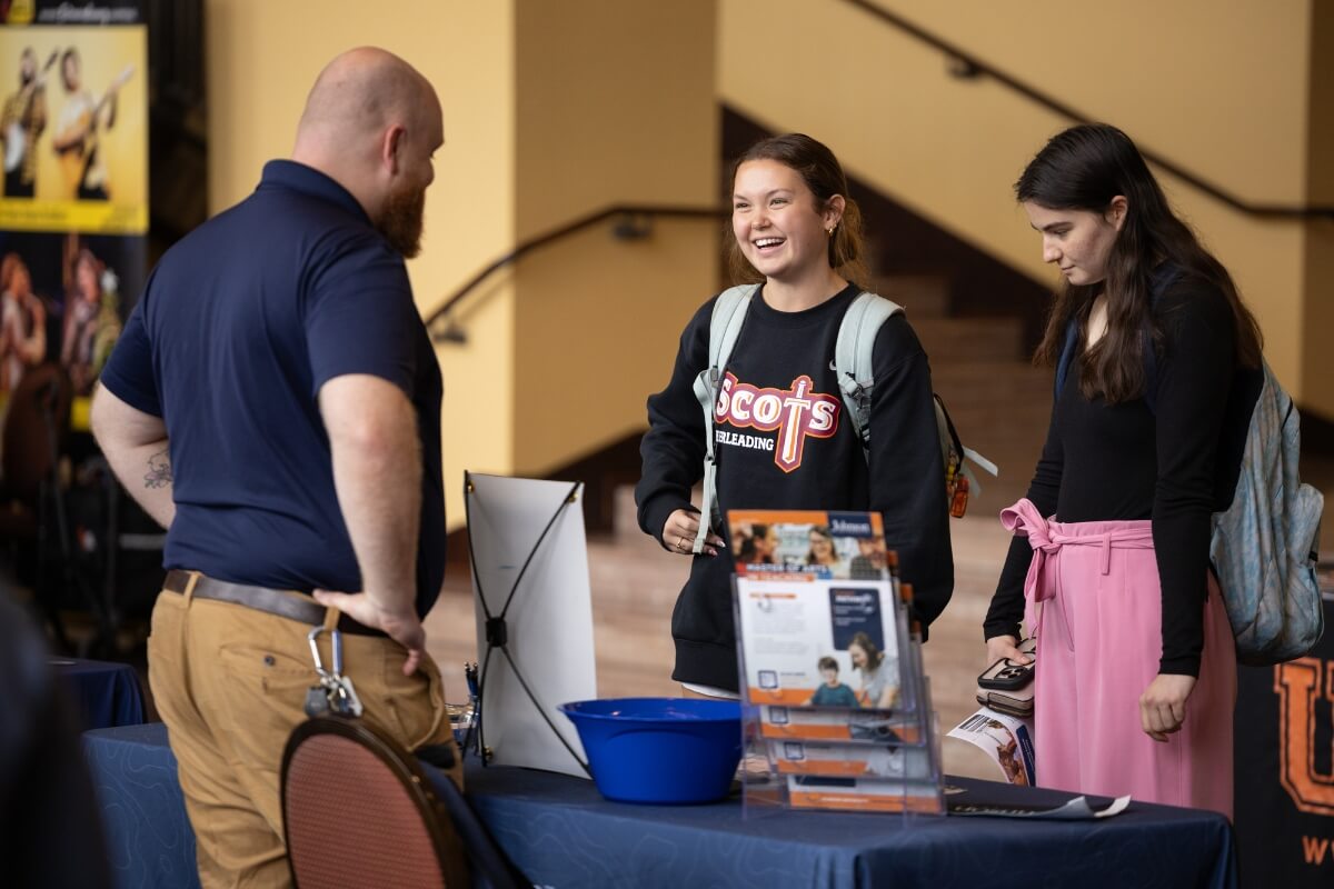 Photo of two women talking to a tall man with his hands on his hips