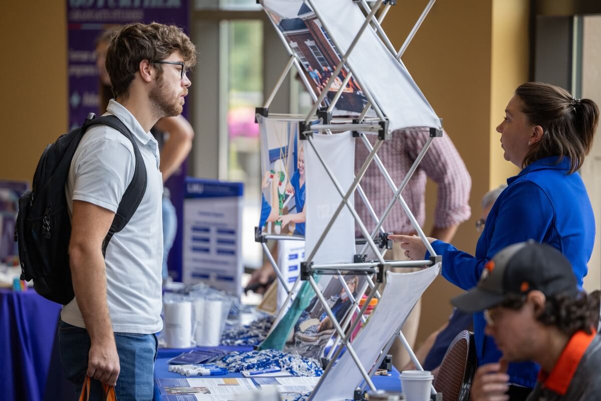 Photo of a student talking to a graduate school representative in the foyer of the Clayton Center for the Arts.