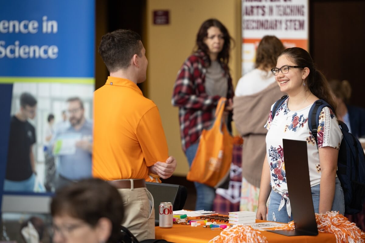 Photo of a smiling girl talking to a man in an orange polo shirt