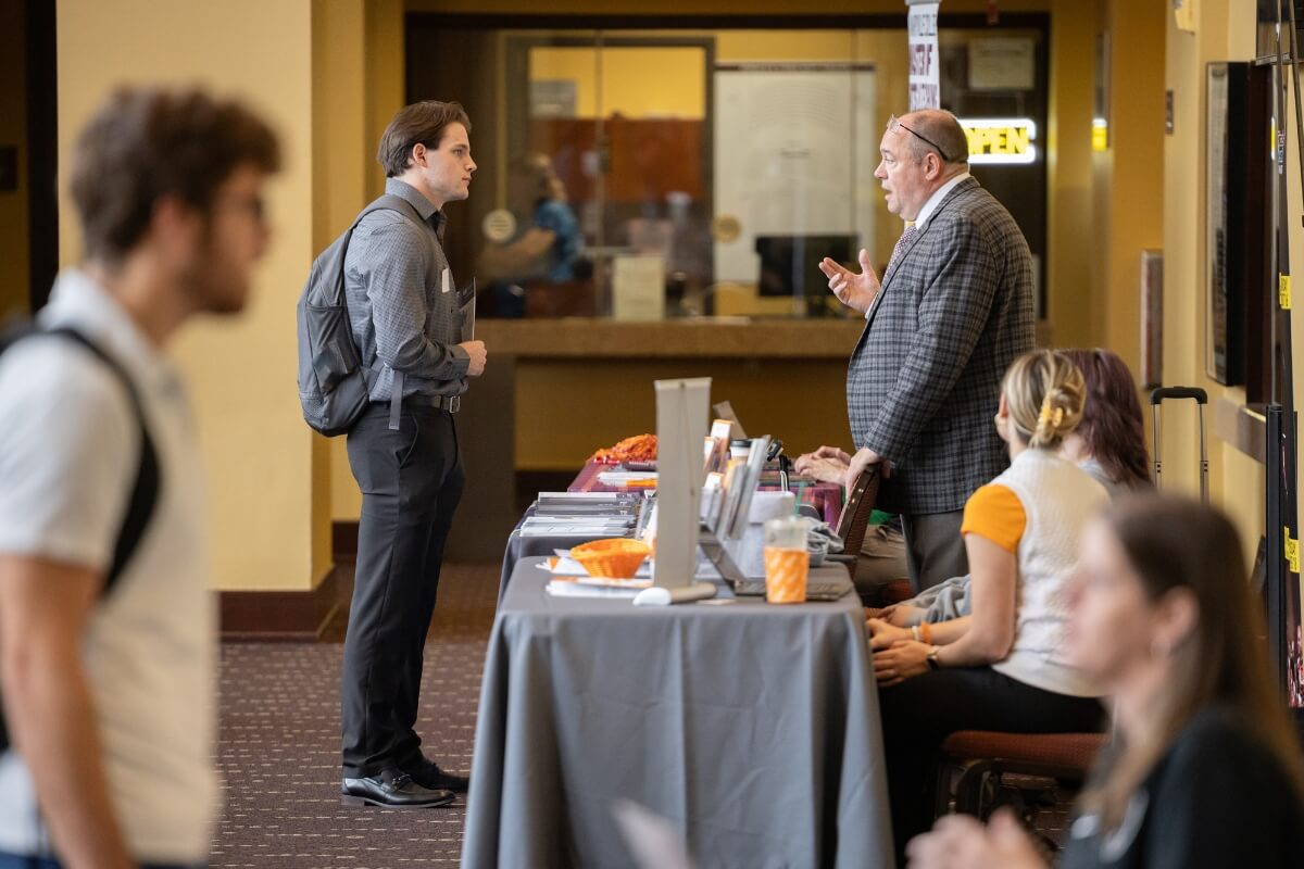 Photo of student talking to graduate school representatives with a blurry person in the foreground