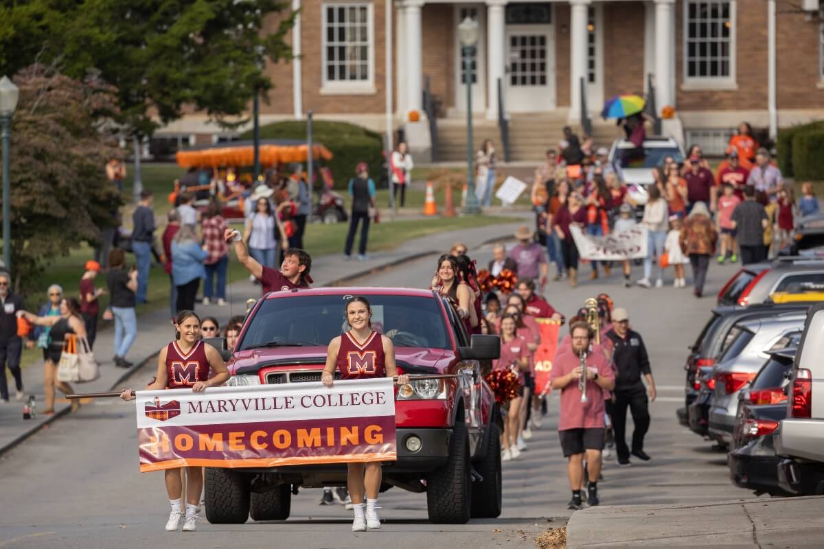 Photo of the front of the Maryville College Homecoming parade, with cheerleaders holding a banner and a crowd of participants behind them