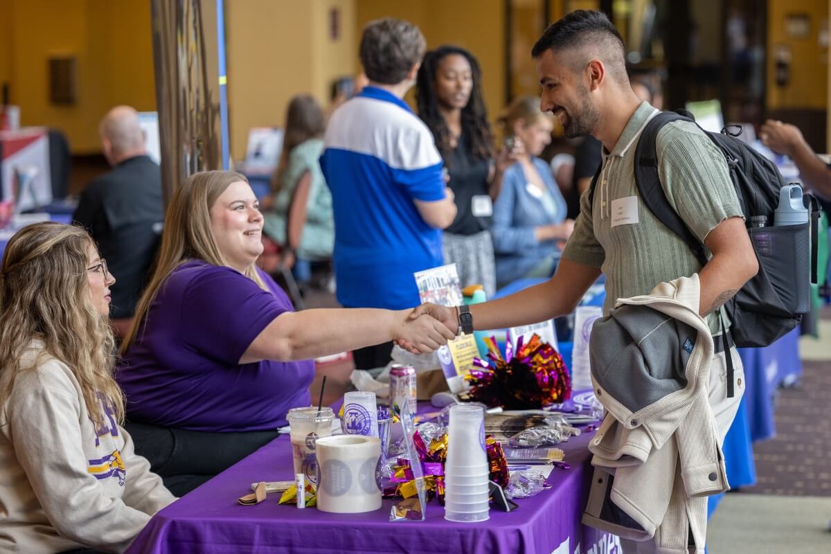 Photo of a seated woman smiling and shaking the hand of a student at the 2025 Maryville College Graduate School and Continuing Education Fair