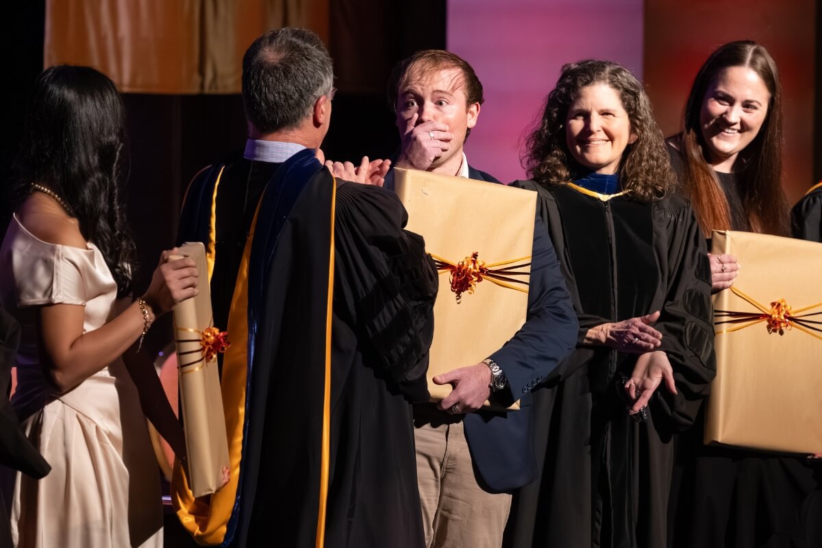 Photo of a guy reacting with shock and surprise as faculty members congratulate him