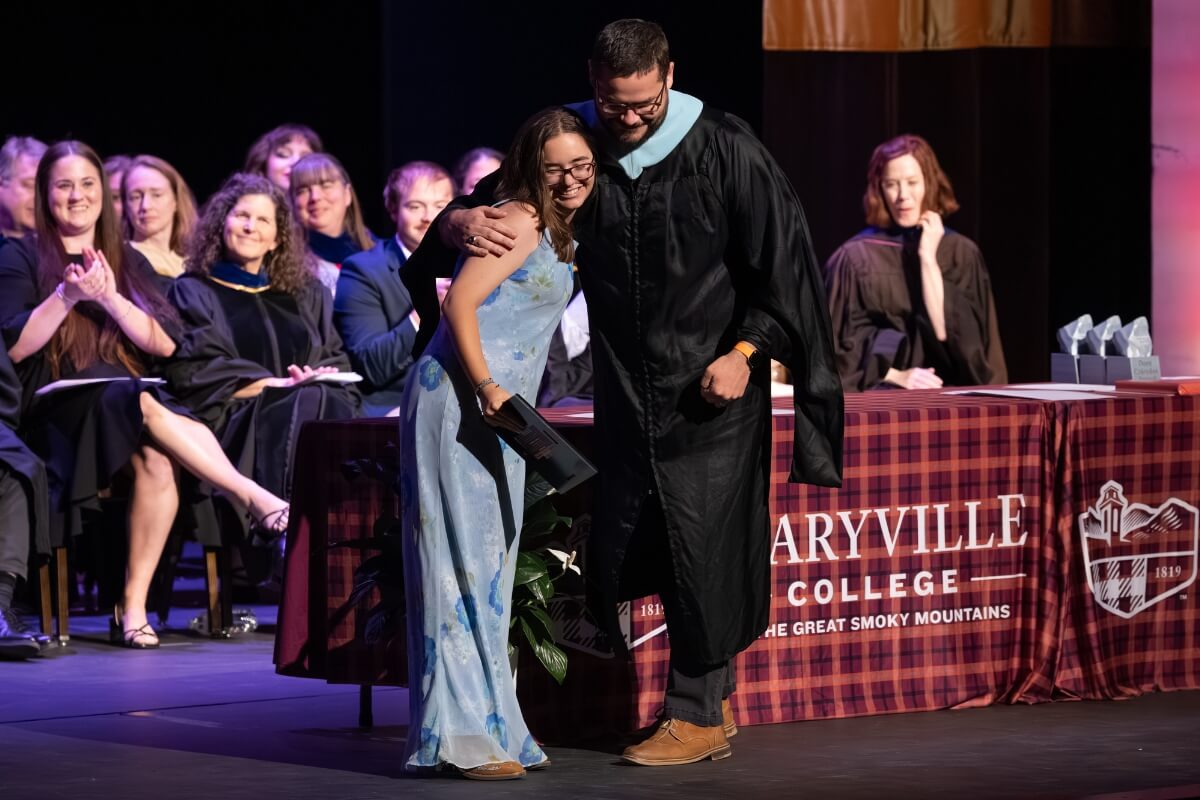 PHoto of a girl holding an award and hugging the guy who presented it to her