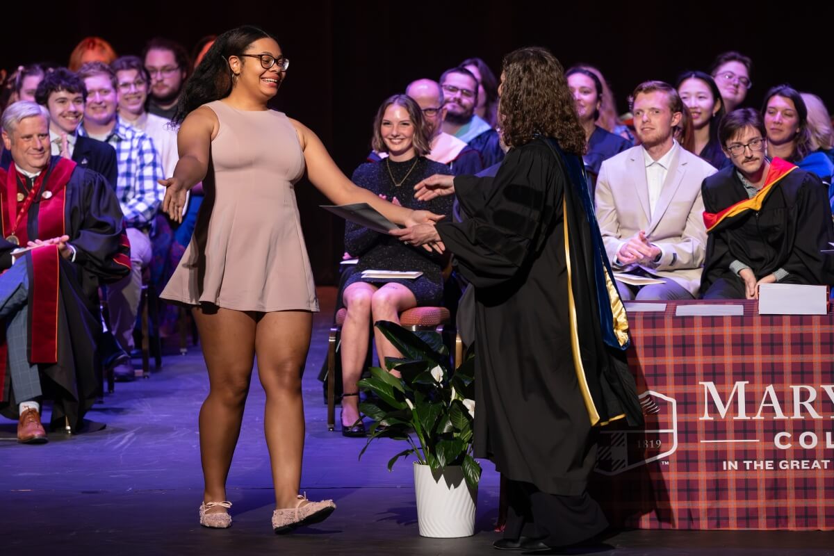 Photo of a girl opening her arms for a hug from a woman in graduation regalia