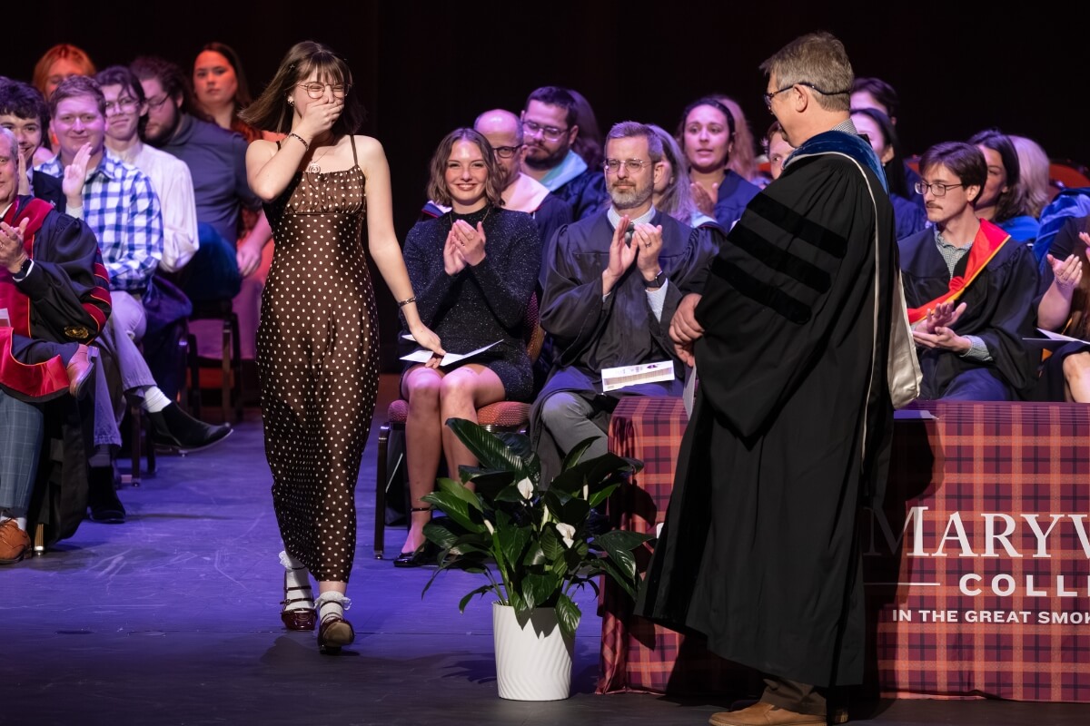 Photo of a girl with her hand over her mouth walking to receive an award