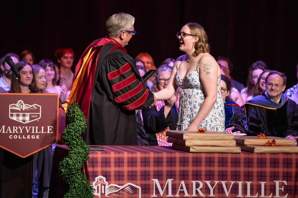 Photo of a girl smiling and shaking hands with a guy in graduation regalia