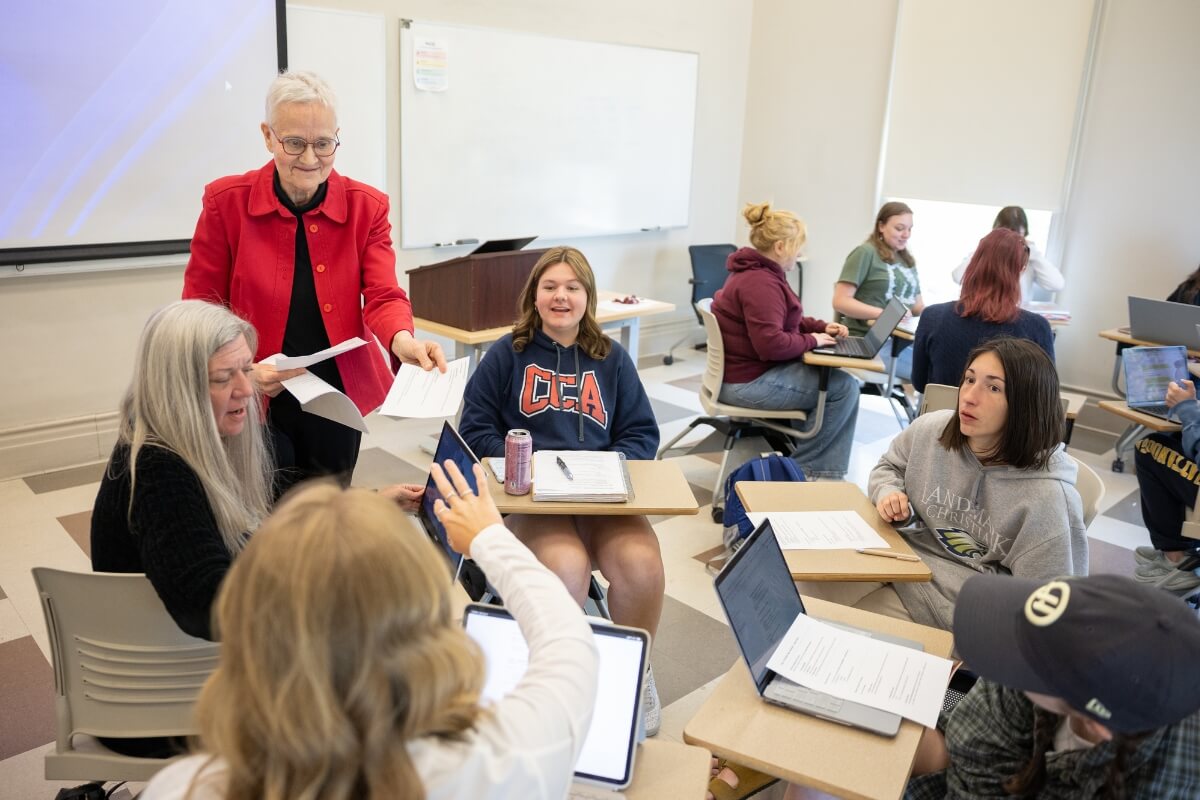 Photo of Jan Taylor handing out papers to students and smiling