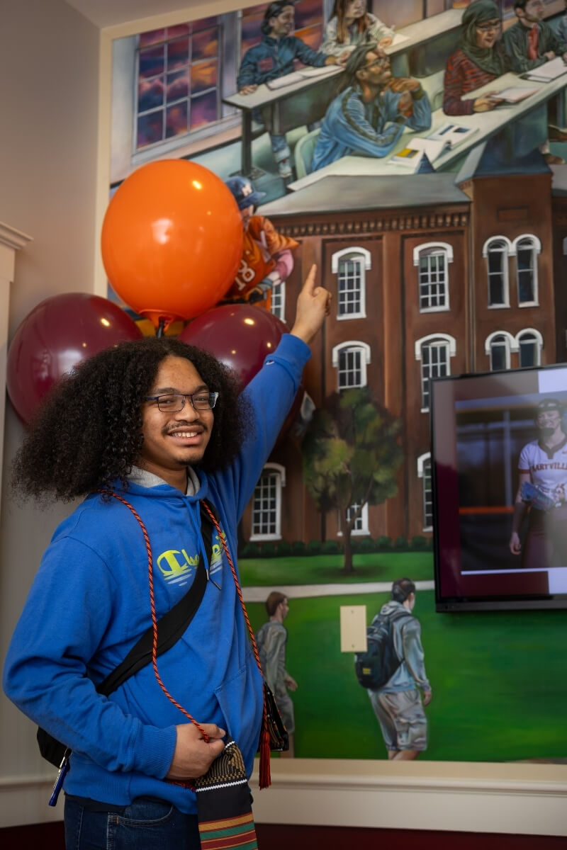 Photo of Lavarius Thenthirath smiling and pointing to an individual in a mural