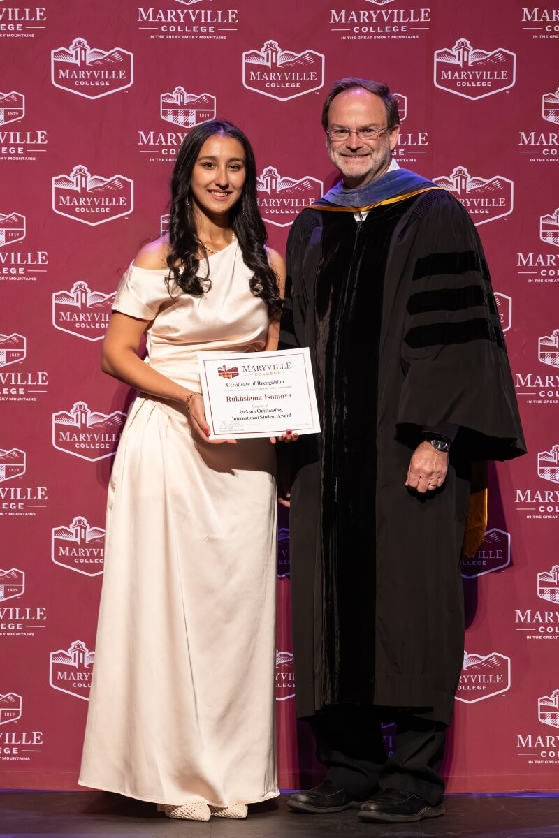 Photo of a young woman holding an award and standing next to a smiling professor in collegiate regaila