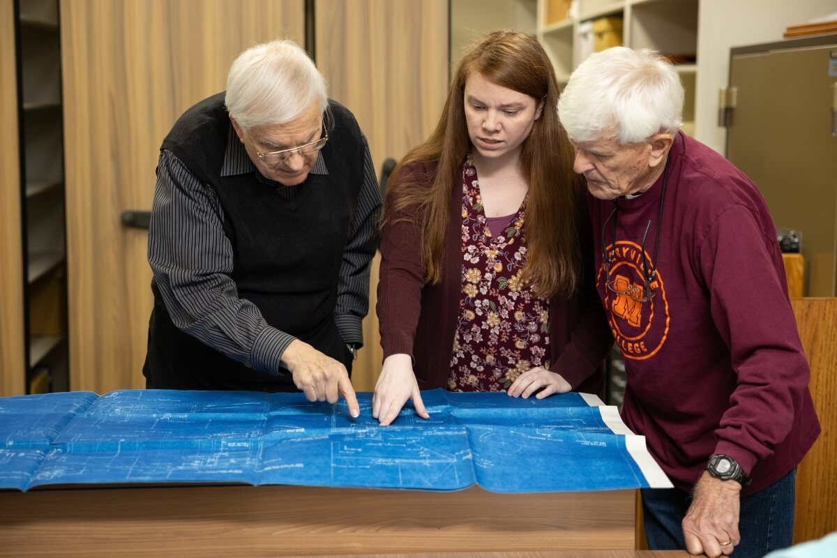 Photo of Amy Lundell '06 looking at blueprints with two College alumni volunteers.