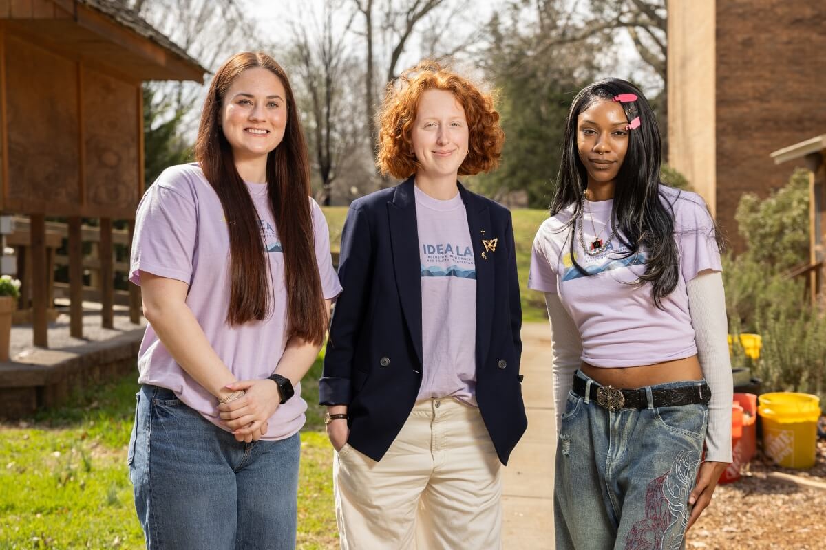 Photo of a professor and two students standing outside on a sunny afternoon