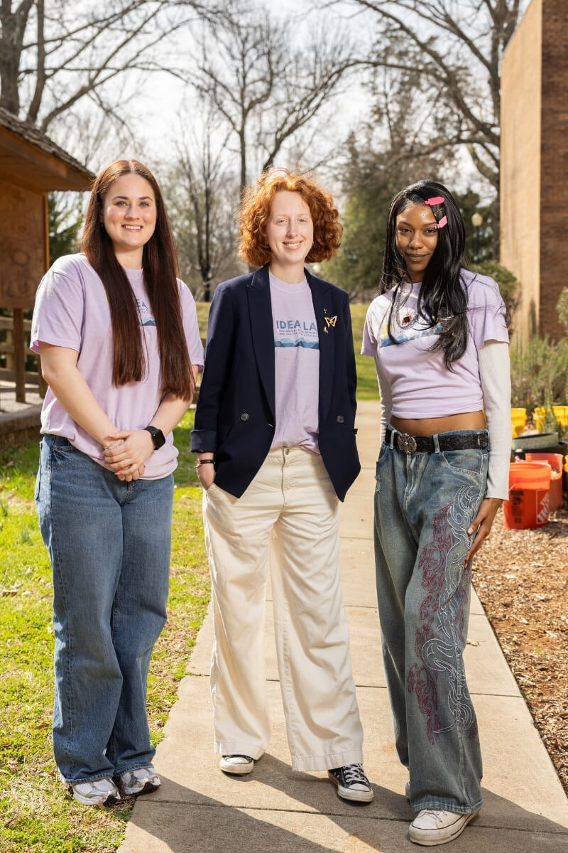 Photo of Dr. Tess Ann Simpson and two students standing outside on a sunny day