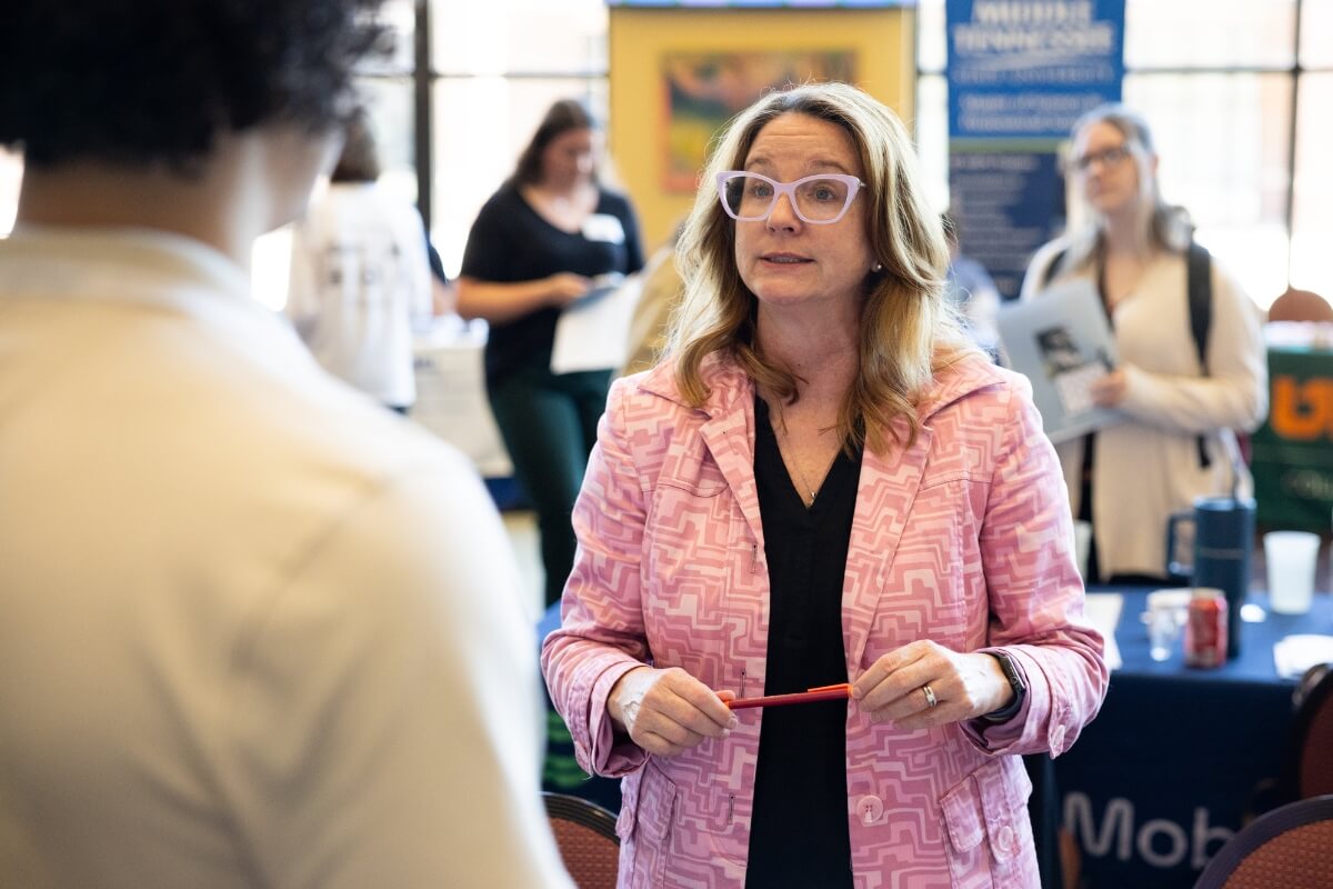 Photo of a woman in a pink jacket and glasses talking with a student at the Maryville College Spring Opportunities Fair
