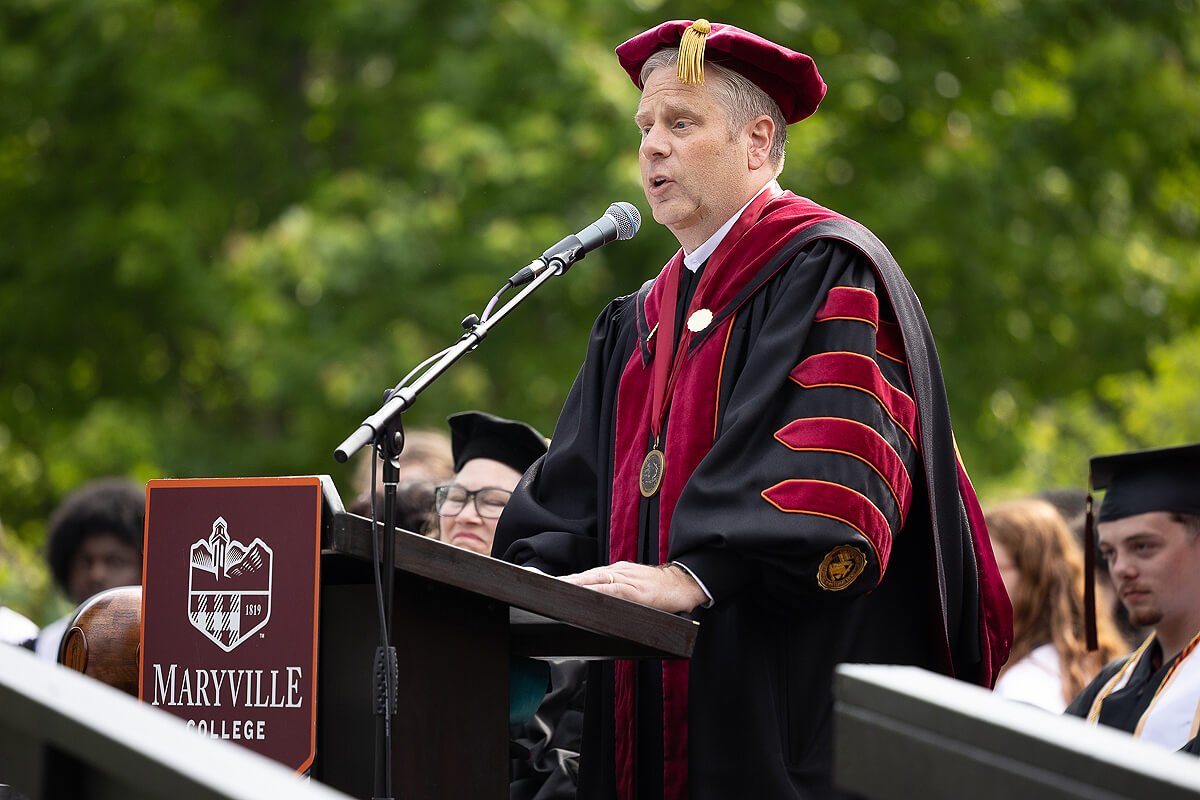 Photo of a man in graduation regalia talking to a crowd