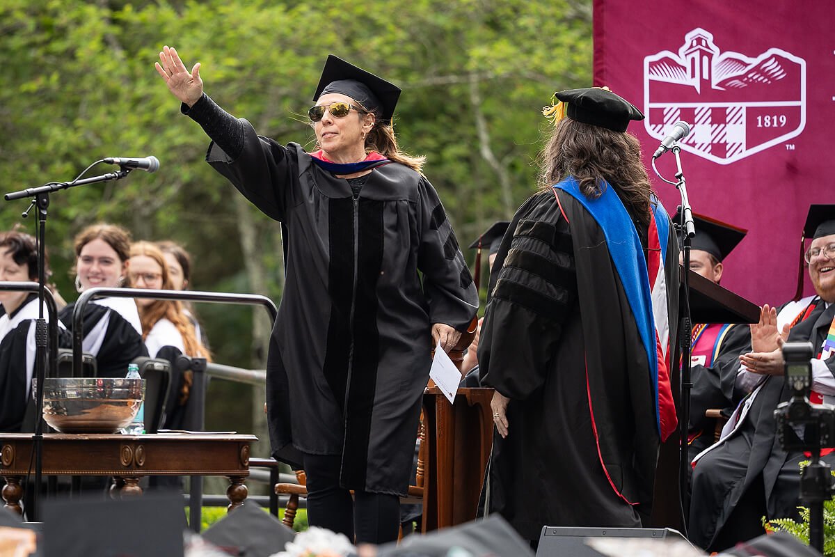 Photo of a woman in graduation regalia saluting the crowd