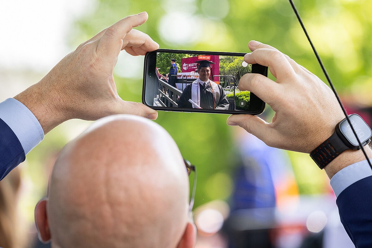 Photo of a man holding a camera and taking a picture of a graduate