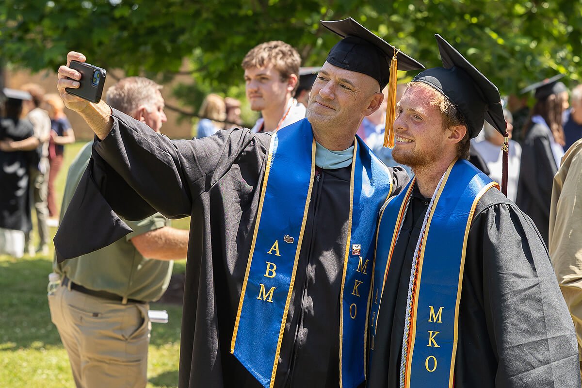 Photo of two young men in graduation regalia taking a selfie