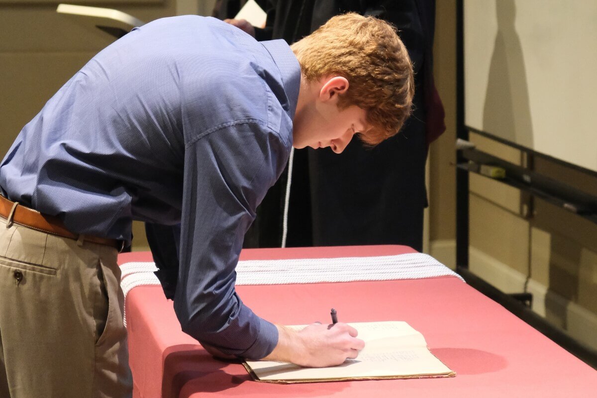 Photo of a young man signing a piece of paper