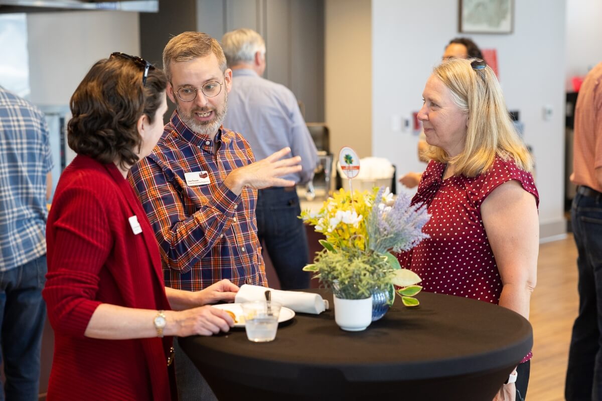 Photo of three people standing around a table, talking