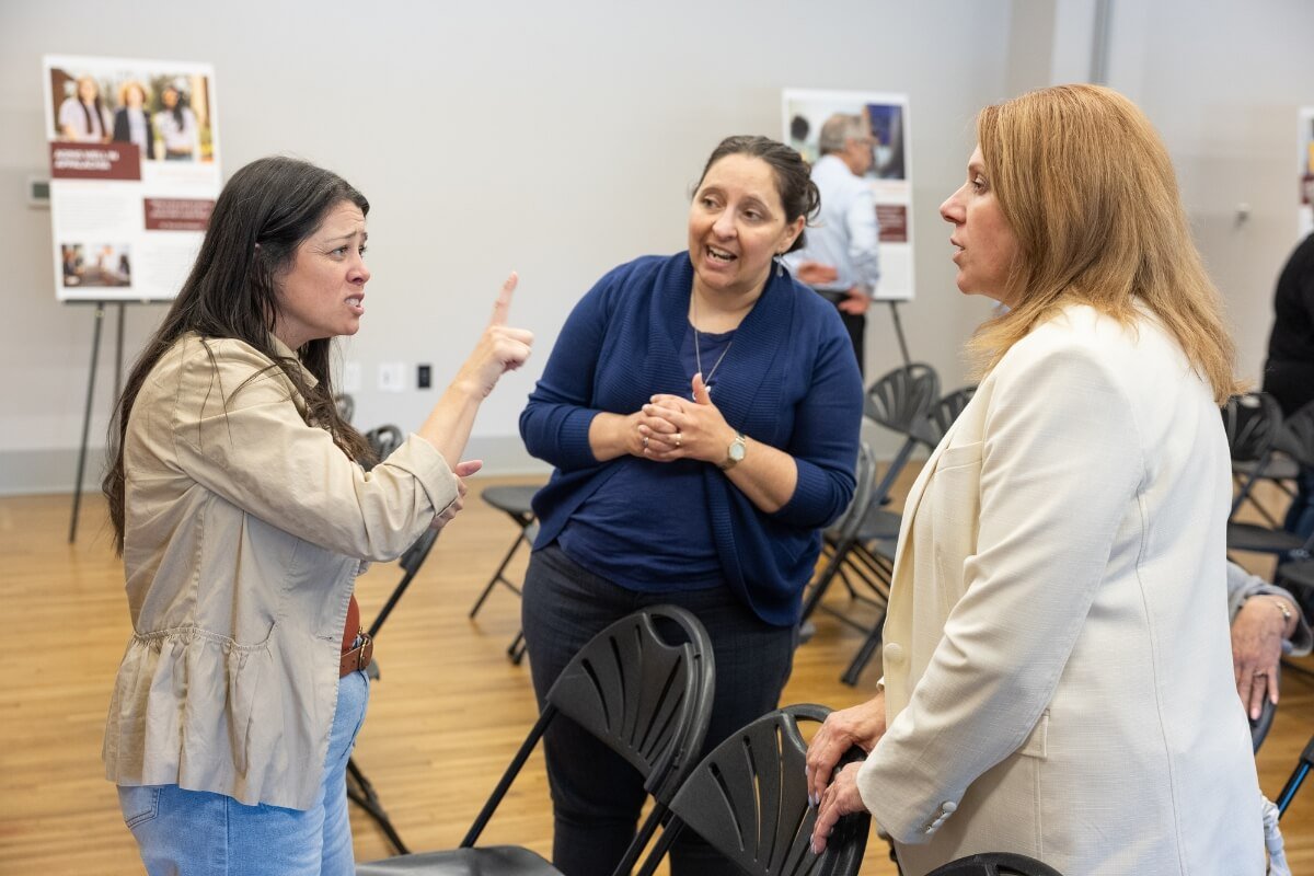 Photo of a Deaf woman signing at another woman while an interpreter translates between them