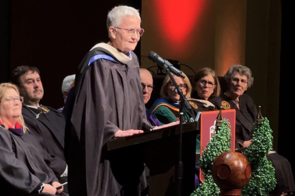 Photo of a woman standing at a lectern wearing graduation regalia