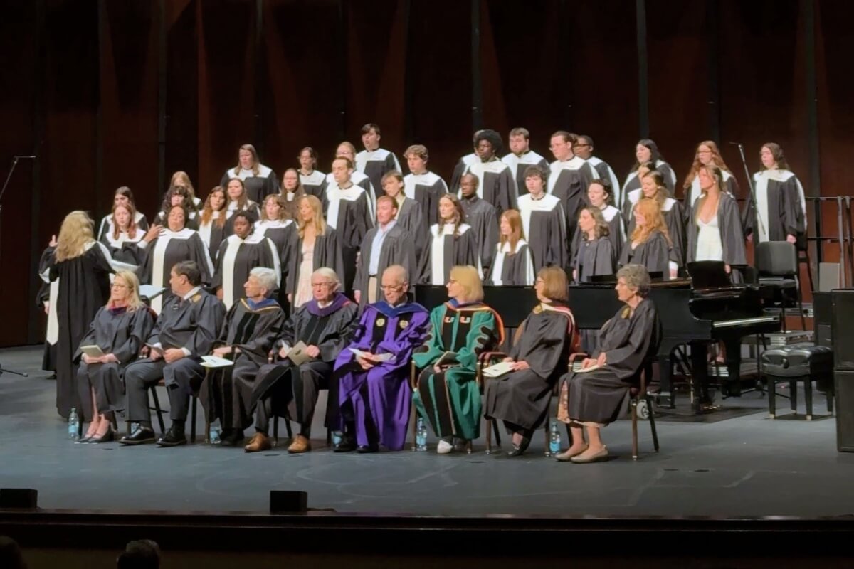 Photo of a choir singing behind a group of people seated on a stage