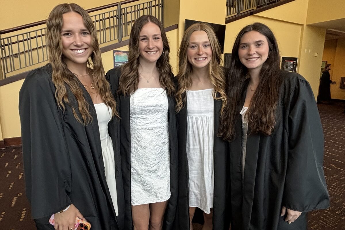 Photo of four smiling young women wearing graduation robes