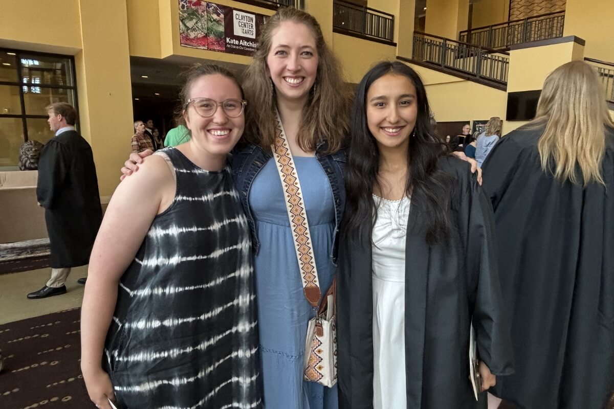 Photo of three smiling women as people mill about behind them
