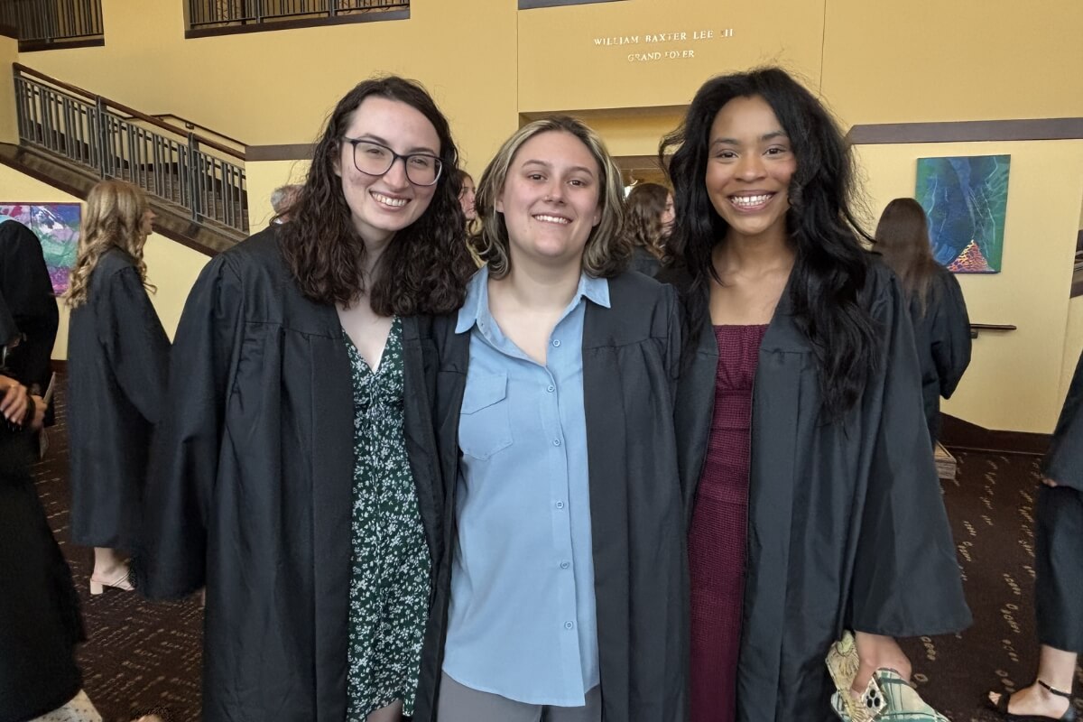 Photo of three smiling young women wearing graduation gowns