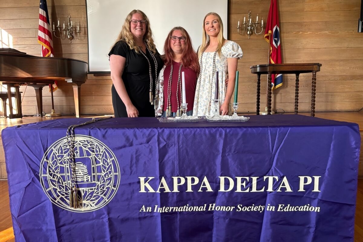 Three women standing in front of a table with a Kappa Delta Pi banner on it