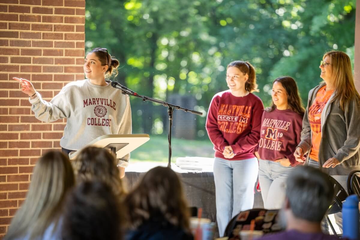 Photo of a woman pointing off-camera and three other women watching her