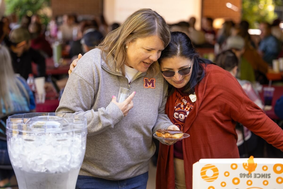 Photo of two women hugging over donuts